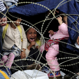 Una niña refuegiada llora tras la alambrada policial que les impide cruzar la frontera entre Grecia y Macedonia.- REUTERS