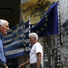 Dos hombres pasean en Atenas por delante de banderas griegas y europeas. /REUTERS
