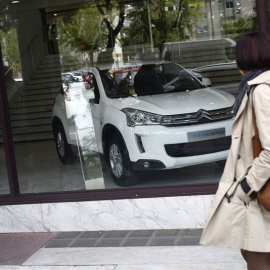 Una mujer pasa junto a un concesionario de automóviles. E.P.