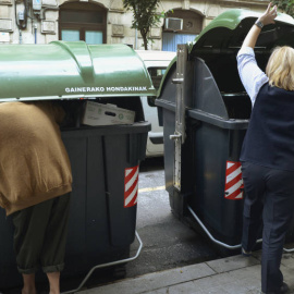 Una persona busca comida en un contenedor de basura de Bilbao, mientras una trabajadora de un supermercado echa bolsas a la basura. REUTERS