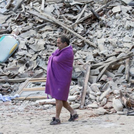 Un hombre que acaba de ser rescatado pasea entre los escombros de la que era su casa/REUTERS