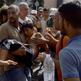 Refugiados llevan en brazos a un niño que se desmayó durante la larga espera para el procedimiento de registro en la isla griega de Lesbos. - EFE
