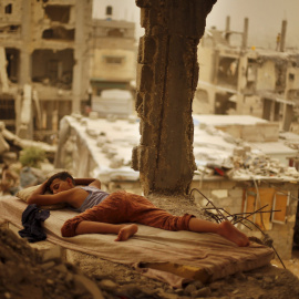 Un niño palestino duerme en un colchón en el interior de los restos de la casa de su familia, que según testigos fue destruida por los bombardeos israelíes durante la guerra de 50 días en el verano de 2014, durante una tormenta de arena en 