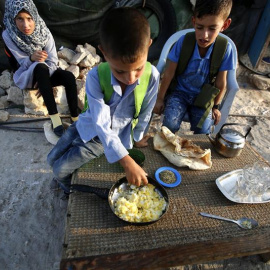 Niños palestinos desayunan antes de ir al colegio en la localidad cisjordana de Susiya. Los alumnos caminan un largo recorrido hasta el colegio debido a la falta de infraestructuras y a la prohibición de Israel de construir un centro educat