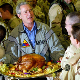 El expresidente de EEUU, George W. Bush, posa para una foto portando un pavo de Acción de Gracias durante su visita a las topas estadounidenses en Bagdad, el 27 de noviembre de 2003. El pavo resultó ser una recreación falsa de plástico.- TI