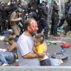 Un migrante herido sostiene a un niño durante los disturbios con la policía húngara en la frontera con Serbia. REUTERS