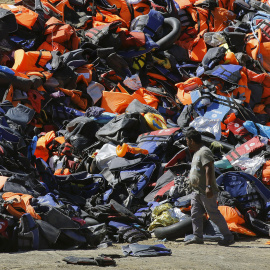 Un hombre pasa junto a una montaña de botes desinflados y chalecos salvavidas dejados por los refugiados tras su llegada a la isla griega de Lesbos. REUTERS