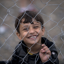 Un niño refugiado sonríe tras las verjas de un campamento mientras espera que otros inmigrantes y refugiados se registren después de cruzar la frontera entre Grecia y Macedonia cerca de Gevgelija el 22 de septiembre de 2015. AFP / NIKOLAY D