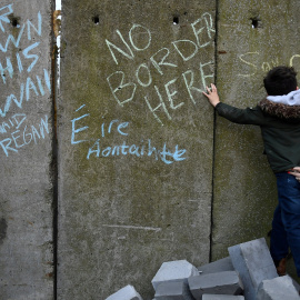 Un niño escribe un mensaje en un muro fronterizo simulado durante una protesta de activistas en contra del brexit, en Irlanda. | Reuters
