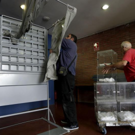 Dos operarios descargan varias urnas e instalan una cabina en un colegio electoral en Barcelona. EFE/Alberto Estévez