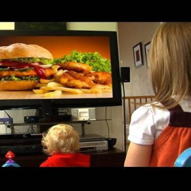 Niños viendo en la televisión un anuncio de comida poco saludable.
