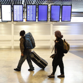 Unos jóvenes buscan su vuelo en los paneles informativos en el aeropuerto dolfo Suárez-Barajas. REUTERS