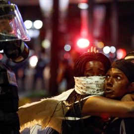 Dos mujeres que abrazan mientras miran a un oficial de policía en la zona alta de Charlotte, Carolina del Norte durante una protesta de los disparos de la policía contra Keith Scott, en Charlotte, Carolina del norte. REUTERS/Jason Miczek