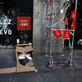 Una mujer sale de una tienda en rebajas mientras un hombre duerme en unas cajas en la calle en Madrid. REUTERS