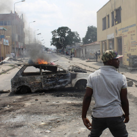 Un hombre junto a un coche quemado en Kinshasa a modo de barricada. - REUTERS