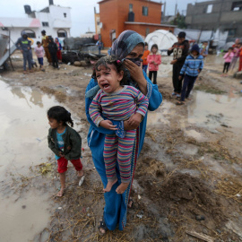 Una mujer palestina lleva a su hija después de que la lluvia inundase su casa que, según testigos, fue dañado por los bombardeos israelíes durante la guerra de 50 días en el verano de 2014, en Khan Younis, en el sur de la Franja de Gaza. RE
