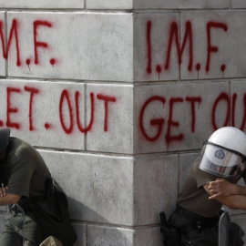 Un par de policías antidisturbios descansan junto a una pintada contra el FMI, durante una manifestación contra las medidas de austeridad (5 de mayo de 2010). REUTERS/Yorgos Karahalis