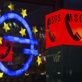Fotografía que muestra el símbolo del Euro reflejado en una ventana junto al letrero luminoso de un teléfono de emergencia, en Fráncfort, Alemania. EFE