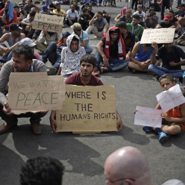 Refugiados con carteles que rezan "Queremos la paz" y "¿Dónde están los derechos humanos?".