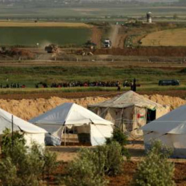 Tiendas gazatíes ‘protegidas’ tras taludes. En el centro, la valla que separa Gaza de Israel. Un poco más allá, los taludes levantados por los sionistas desde donde asesinan impunes a los gazatíes que se ponen a tiro seguro.