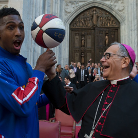 El Obispo Dominick Lagonegro gira una pelota de baloncesto en el dedo con la ayuda de los Harlem Globetrotters frente a la Catedral de San Patricio durante el desfile del día de Colón en la ciudad de Manhattan de Nueva York. REUTERS / Steph