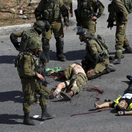 Soldados israelíes rodean a un compañero que yace en el suelo tras ser acuchillado por un joven palestino (d), que fue abatido posteriormente, en la ciudad palestina de Hebró. EFE/Abed Al Haslhamoun