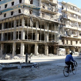 Un hombre pasa en bicicleta por un edificio destrozado por las bombas en Alepo. /REUTERS