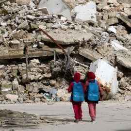 Dos niñas con mochilas donadas por UNICEF pasan junto a un edificio derruido en Alepo de camino a la escuela. Fotografía de marzo de 2015. - ZEIN AL-RIFAI (AFP)