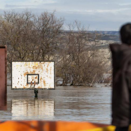 Varias personas observan un campo de baloncesto anegado por la crecida del río Ebro, hoy en la localidad de Cabañas de Ebro. Las motas de contención están aguantado el caudal del Ebro y la noche ha transcurrido en los pueblos de la ribera z