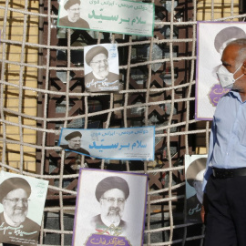  Un partidario del candidato presidencial iraní Ebrahim Raisi camina junto a sus carteles durante un mitin de campaña electoral en la capital, Teherán, el 10 de junio de 2021.- AFP