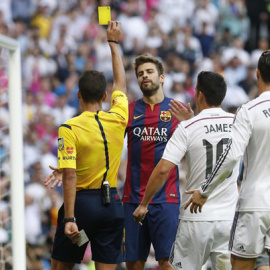 Gil Manzano le enseña una amarilla a Piqué ante Cristiano y James en el clásico del año pasado. /EFE