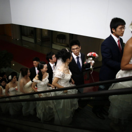 Parejas chinas suben por una escalera mecánica antes de participar en una boda masiva. en  Shanghai, en mayo de  2013. REUTERS/Carlos Barria