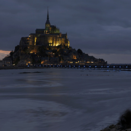 La gente se sienta en un terraplén para observar como la marea  rodea la abadía de Mont Saint-Michel, del siglo XI,en Normandía. REUTERS / Pascal Rossignol