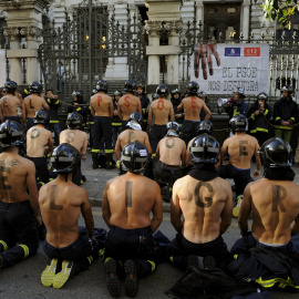 Varios bomberos participan en una protesta frente al parlamento regional de Asturias exigiendo mejores salarios y mayores estándares de seguridad pública en Oviedo, España, 19 de noviembre de 2015. Las letras pintadas sobre las espaldas de 
