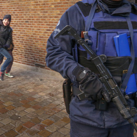 Dos niños saludan a la cámara con un salto detrás de un oficial de la policía belga que está de guardia a las afueras de una escuela en el centro de Bruselas, 25 de noviembre de 2015. REUTERS / Yves Herman