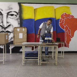 Un trabajador del Consejo Nacional Electoral perpara la máquina de votación junto a un mural con la imagen del expresidente venezolano Hugo Chavez, en un colegio de Caracas. REUTERS/Marco Bello