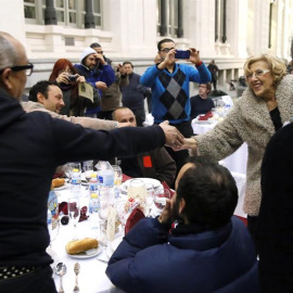 La alcaldesa de Madrid, Manuela Carmena (d), saluda a algunas de las 200 personas sin hogar que esta noche cenan en el Palacio de Cibeles, organizadas por la Fundación Mensajeros de la Paz que preside el padre Ángel en colaboración con el A