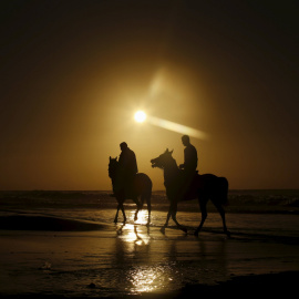 Unos palestinos pasean a caballo por la orilla de la playa en el atardecer de Gaza. REUTERS/Mohammed Salem