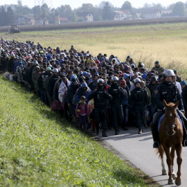 Un policía guía a un grupo de refugiados hacia la entrada del campo de Dovoba, en Eslovenia./ REUTERS