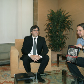 El presidente de la Generalitat, Carles Puigdemont, junto al líder de Podemos, Pablo Iglesias, quien sostiene el libro sobre Andreu Nin que le ha regalado. EFE/Andreu Dalmau