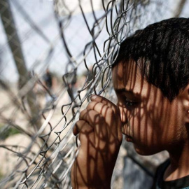 Un niño se apoya en una valla durante una manifestación por la apertura de las fronteras a Macedonia en el campo improvisado de refugiados de Idomeni. / KOSTAS TSIRONIS (EFE)