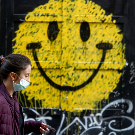  Una joven con mascarilla pasa por delante de una tienda cerrada, con un dibujo de un 'smiley' en su fachada, en Madrid. REUTERS/Sergio Perez