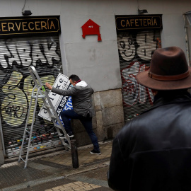 Un hombre se prepara para colgar el cartel de 'Disponible' en el local de una cafetería cerrada durante la pandemia del coronavirus, en el centro de Madrid. REUTERS/Susana Vera