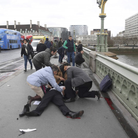 Varias personas atienden a uno de los heridos en el puente frente al Parlamento / REUTERS