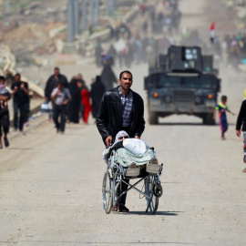 Un desplazado iraquí de Mosul por los combates entre el Ejército y el Estado Islámico lleva a una mujer en silla de ruedas.-REUTERS/Khalid al Mousily