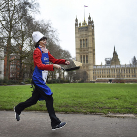 Una parlamentaria corre mientras da la vuelta a una tortita por los jardines de Victoria junto a las Casas del Parlamento en Londres, durante la tradicional carrera de tortitas para recaudar dinero para obras de caridad. EFE/Andy Rain