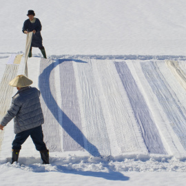 Una pareja coloca tela de kimonos sobre la nieve para su limpieza en Shiozawa en la prefectura de Niigata en Japón. EFE/Everett Kennedy Brown
