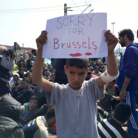 Un niño refugiado sostiene un cartel mientras refugiados y migrantes participar en una protesta contra el cierre de la frontera entre Grecia y Macedonia. REUTERS/Fedja Grulovic