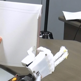 El sujeto amputado sostiene un cuaderno usando la prótesis de mano mioeléctrica con control de sinergia muscular
