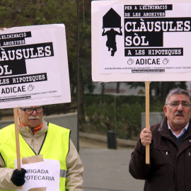 Imatge de dos membres d'Adicae amb pancartes aquest dimecres 9 de març a tocar de la Ciutat de la Justícia de l'Hospitalet. (Horitzontal)